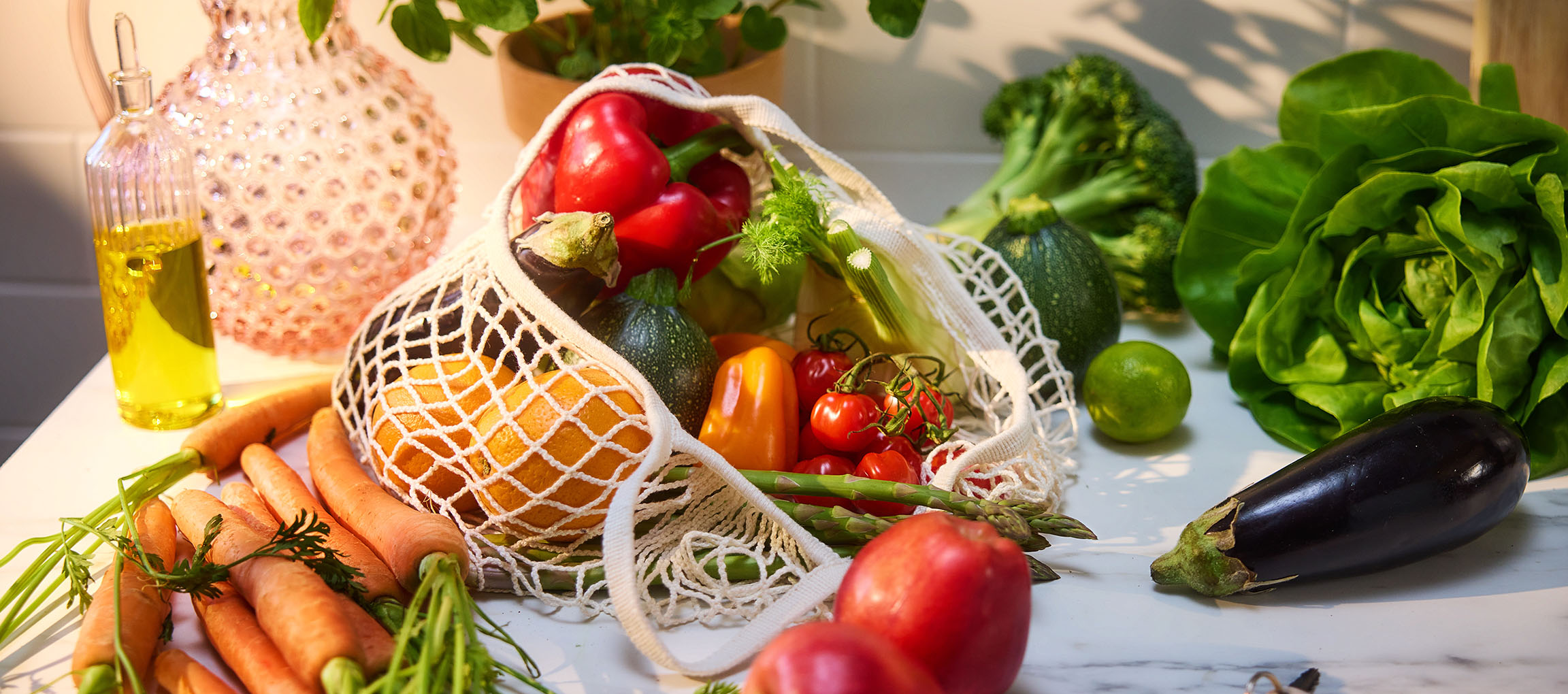 Frisches Gemüse und Obst, darunter Karotten, Paprika, Tomaten, Salat und Aubergine, auf einem Tisch.
