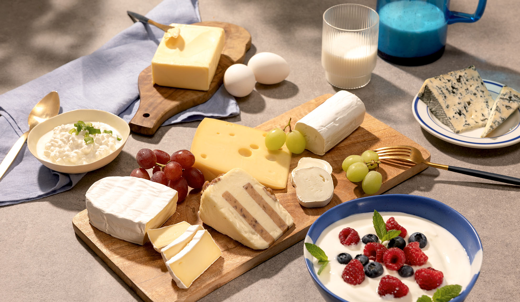 Eine Auswahl an Käse, Trauben und Milchprodukten wie Hüttenkäse, Milch und Joghurt mit Beeren.