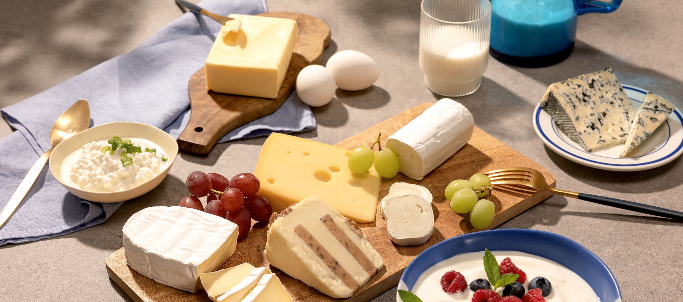 Verschiedene Käsesorten, Eier, Trauben, Milch und Joghurt mit Beeren auf einem Tisch.