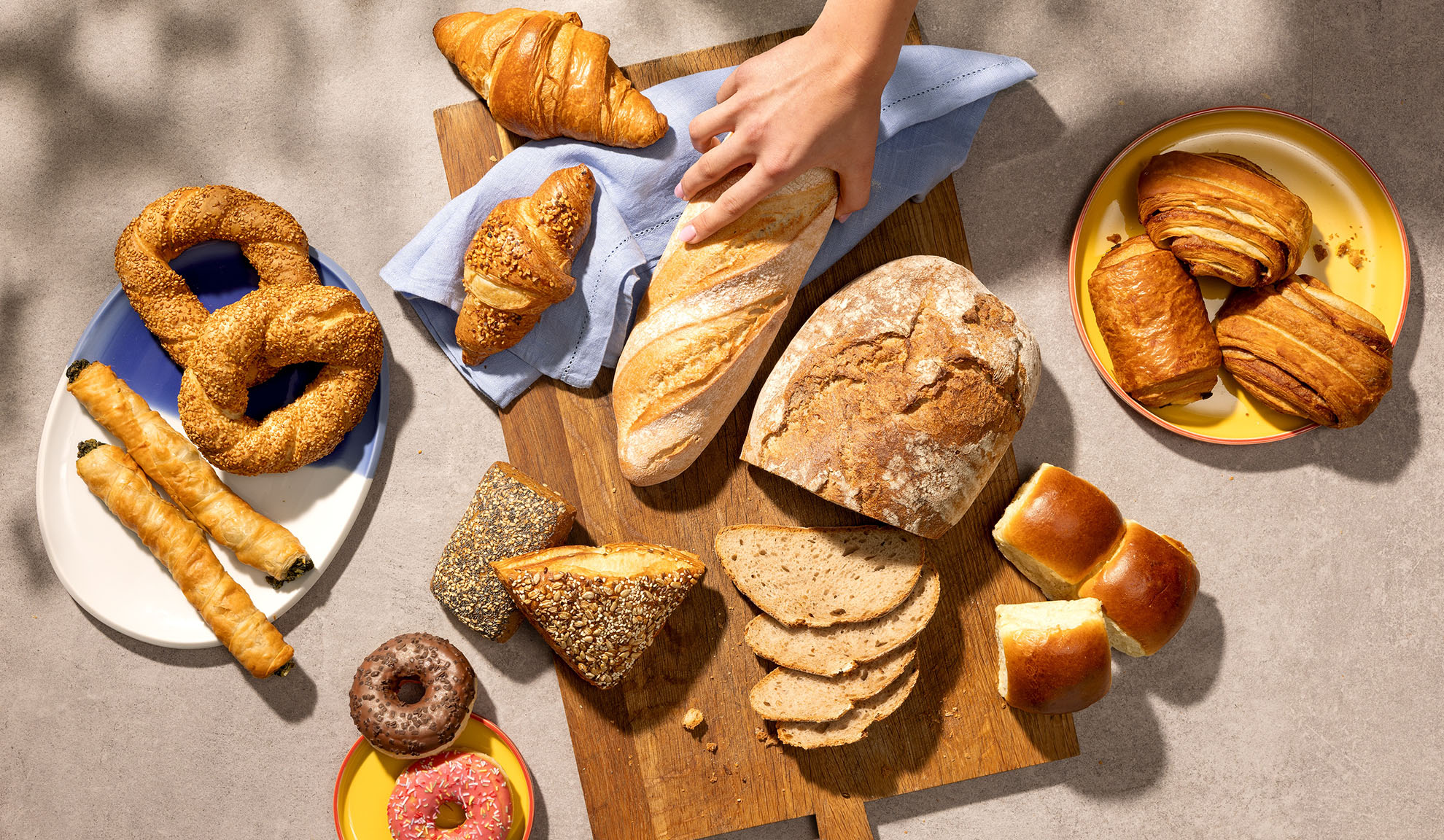 Auswahl an frischen Backwaren, darunter Brot, Croissants, Gebäck und Donuts auf einem Tisch.