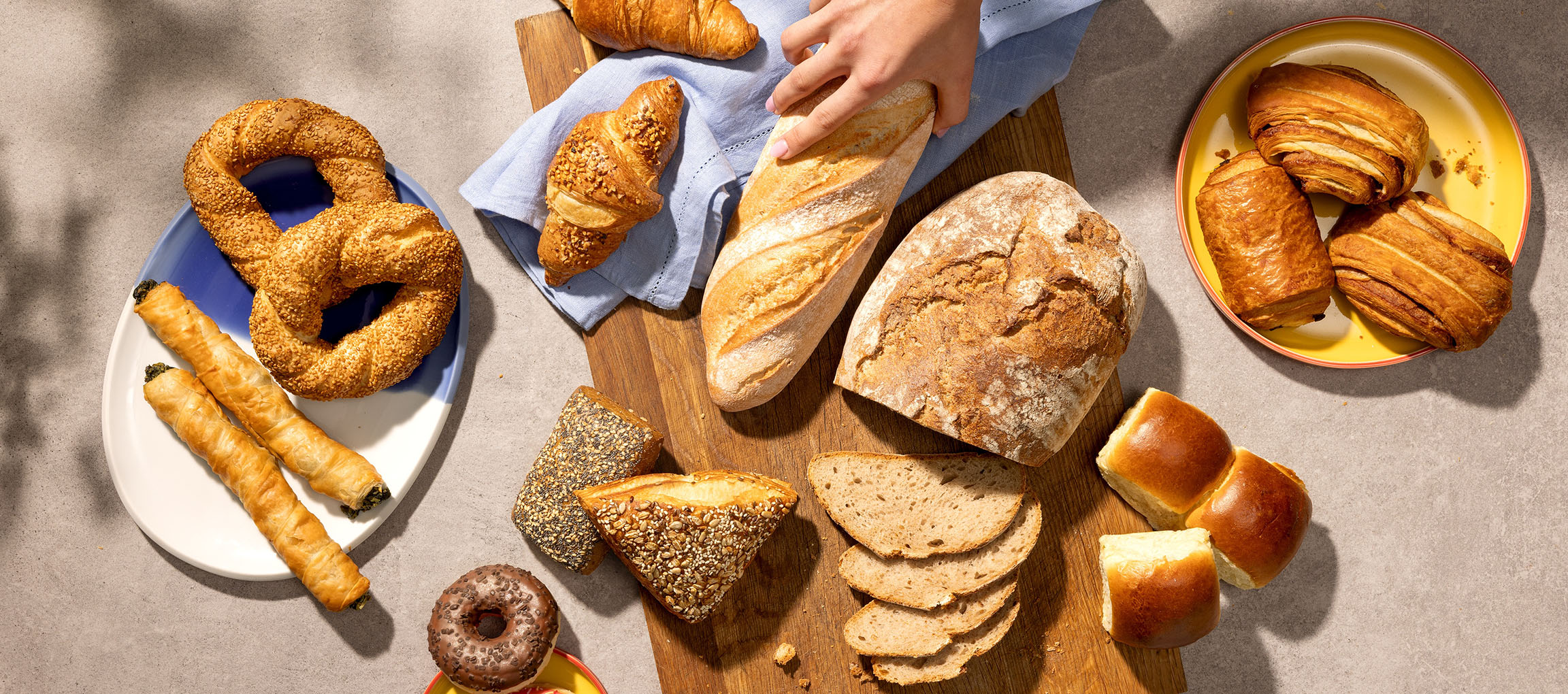 Auswahl an Gebäck und Brot, darunter Brezeln, Croissants und Baguettes, auf einem Tisch.