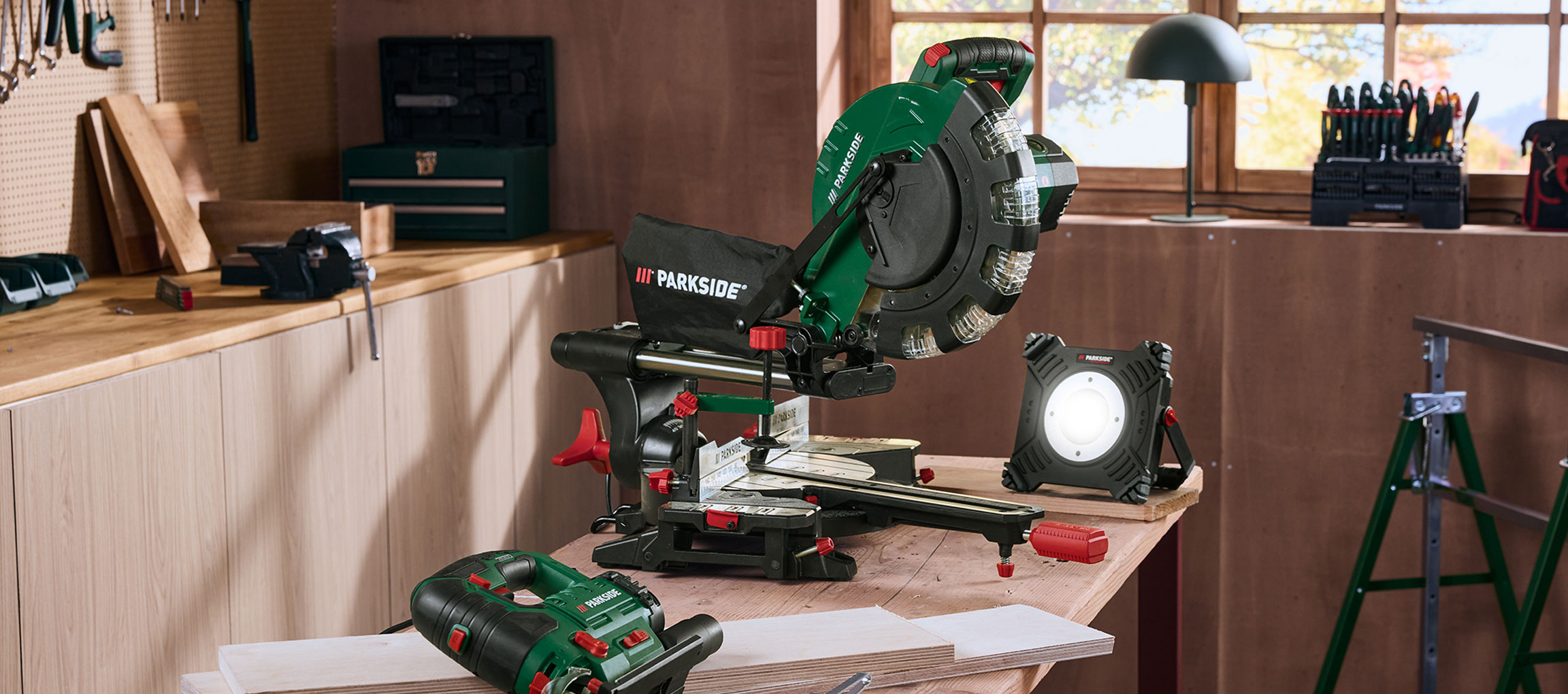 Werkstatt mit Kappsäge, Arbeitsleuchte und anderen Werkzeugen auf einem Holztisch.