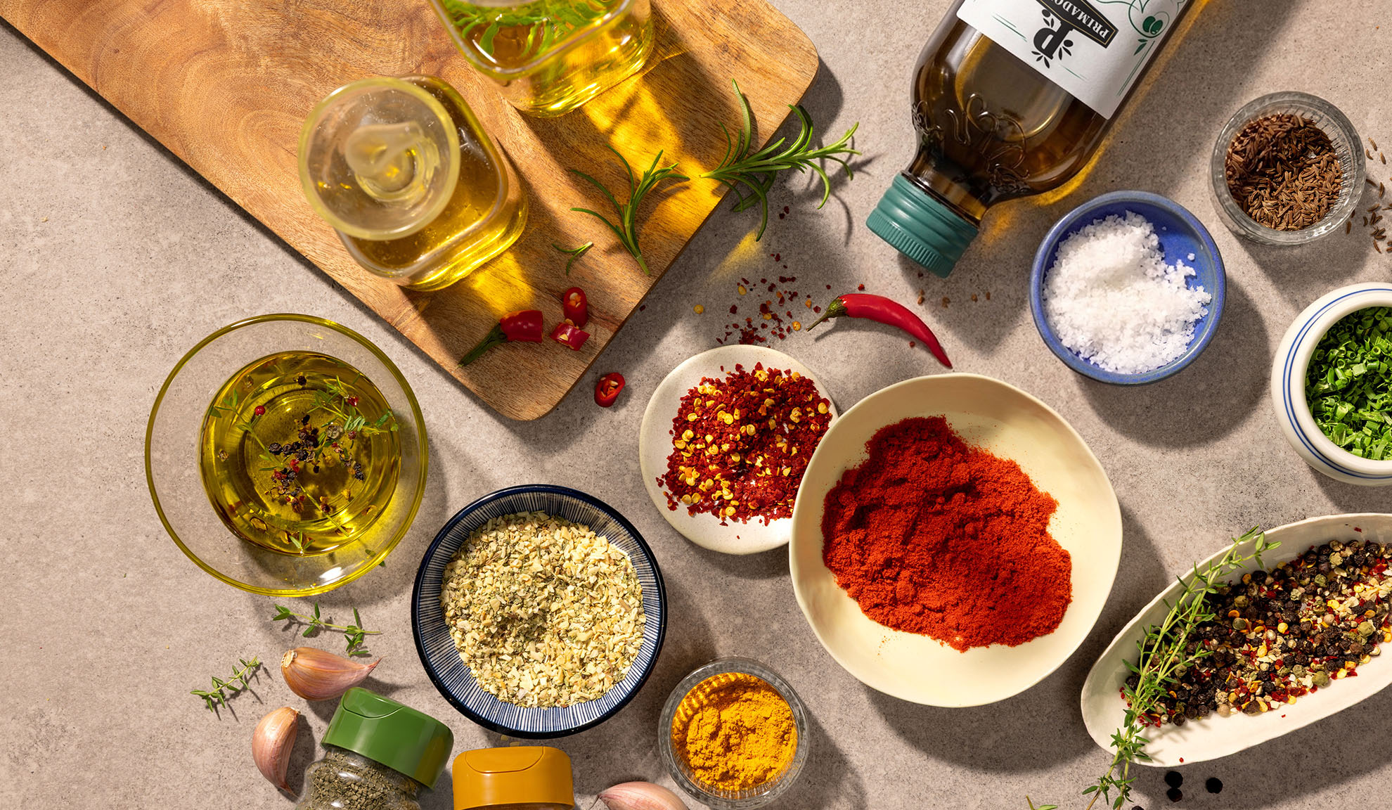 Olivenöl, Gewürze und Chilischoten auf einem Holzschneidebrett und einer Betonarbeitsplatte.