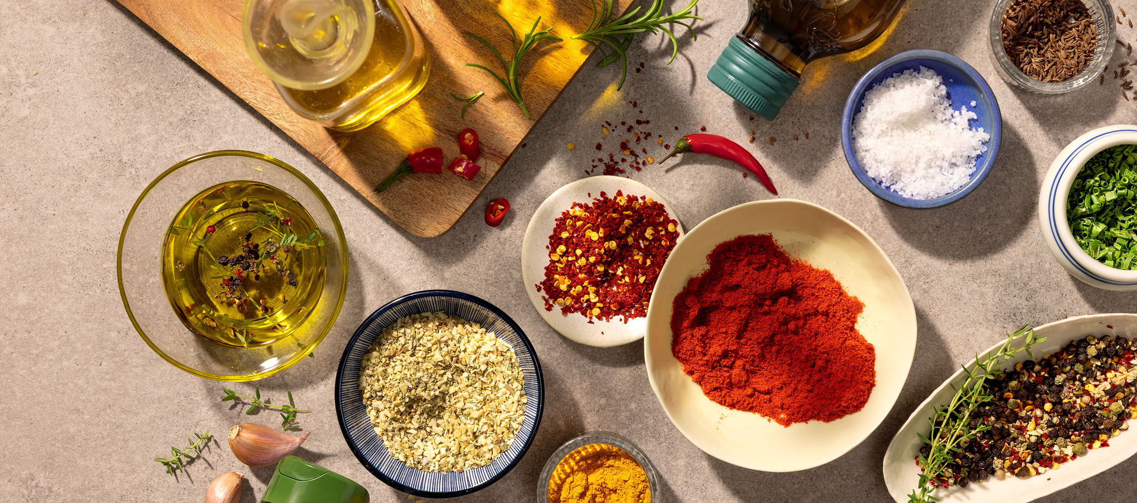 Olivenöl, Gewürze und Chilischoten auf einem Holzbrett und Steintisch.