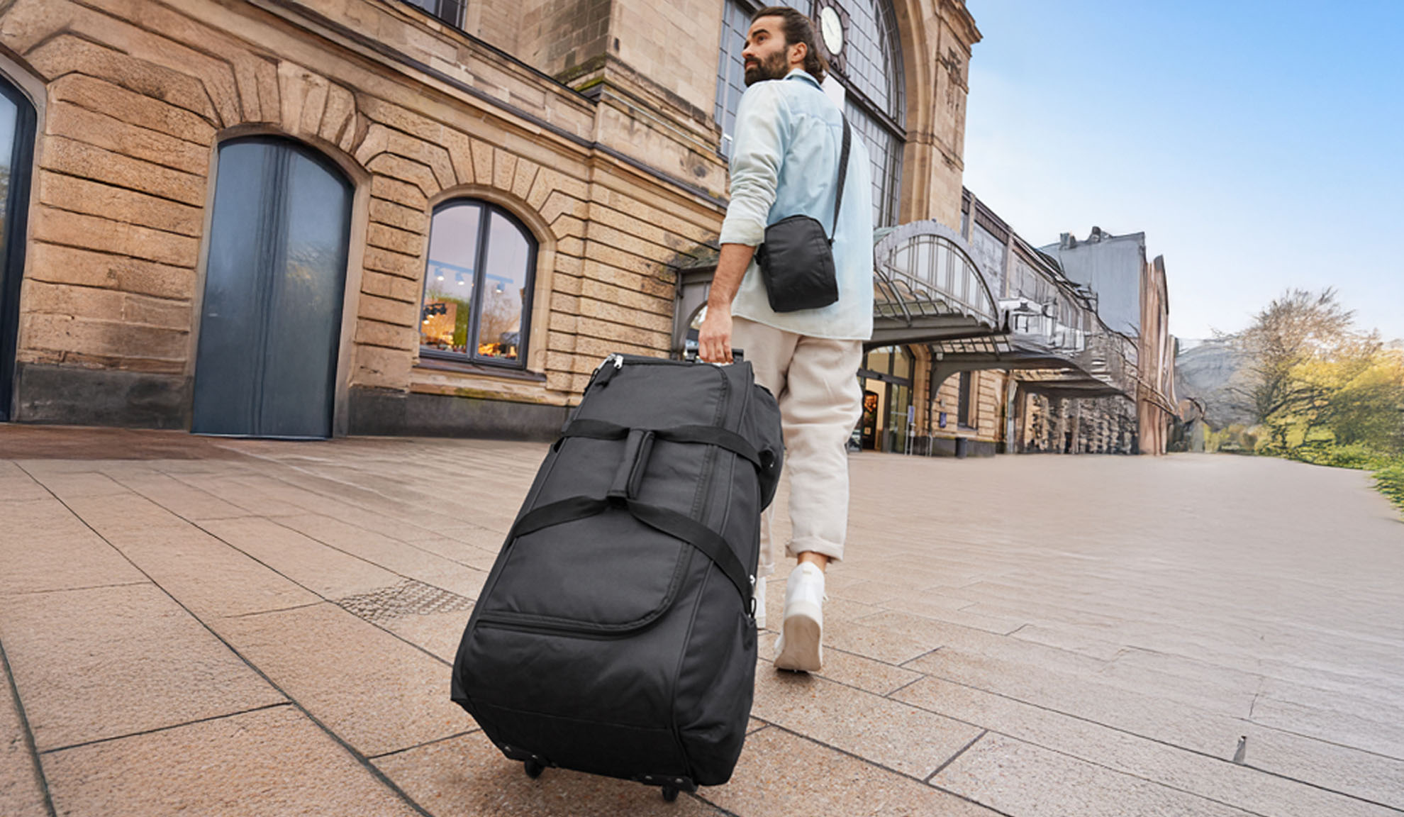 Ein Mann geht mit einem Rollkoffer an einem Bahnhof entlang.