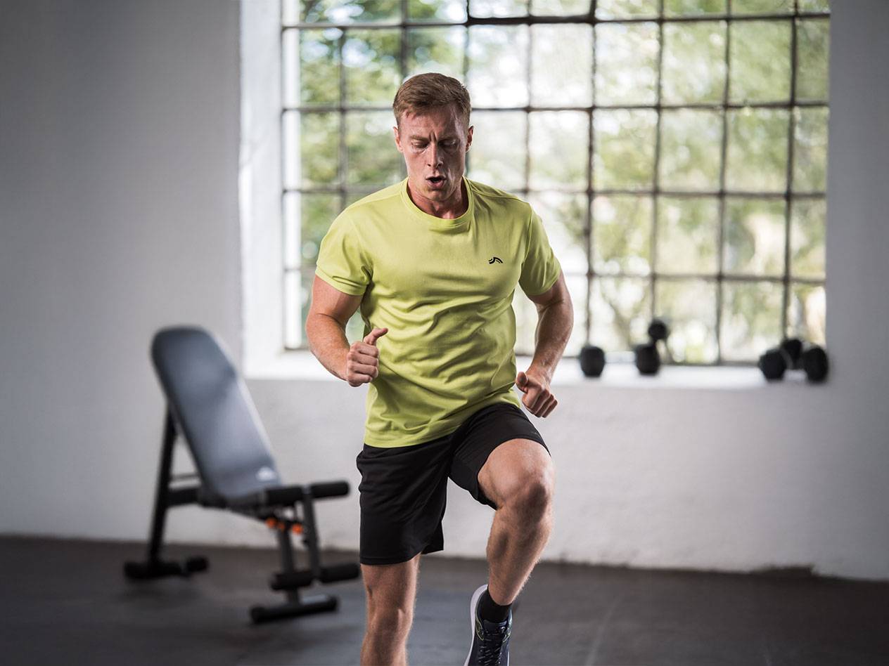 Mann in gelbem T-Shirt und schwarzen Shorts läuft in einem Fitnessstudio.