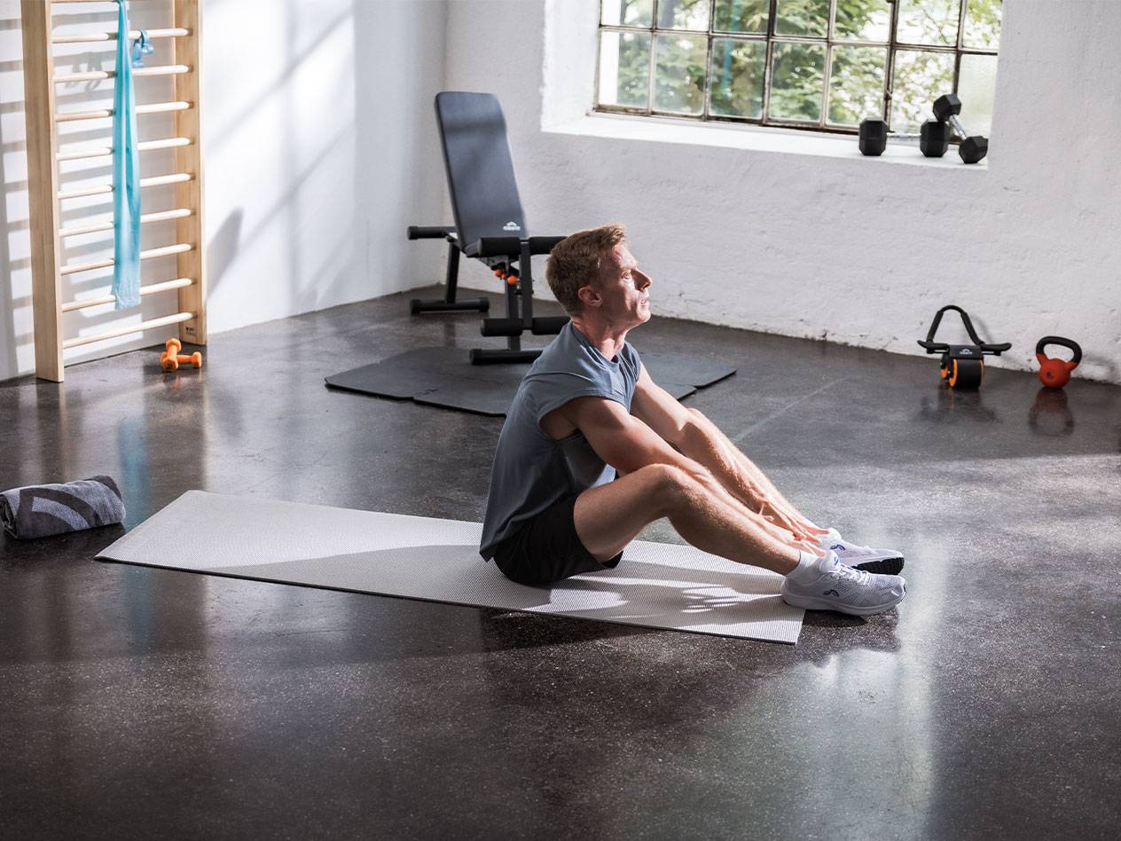 Ein Mann dehnt sich auf einer Yogamatte in einem Fitnessstudio mit Geräten.