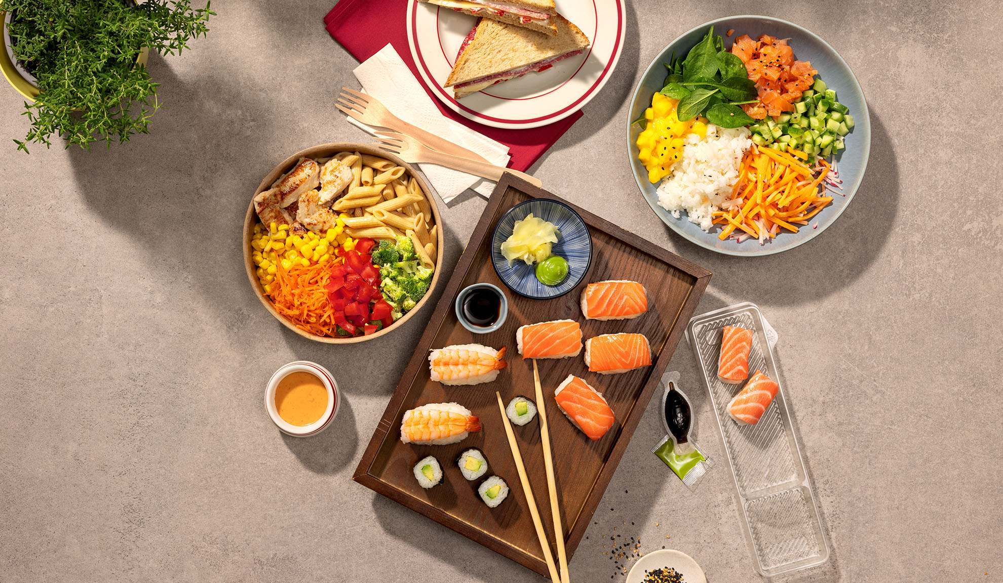 Aufsicht auf verschiedene Takeaway-Mahlzeiten: Sushi, Poke Bowl, Nudelsalat und Sandwiches.