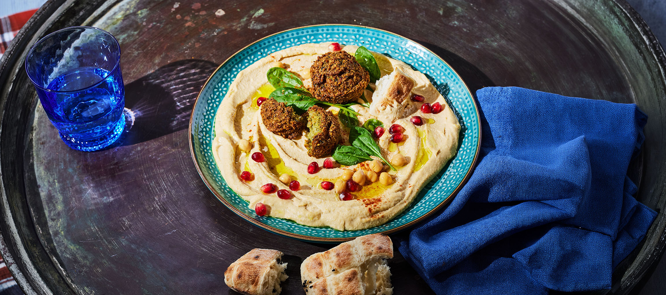Hummus mit Falafel, Granatapfelkernen und Brot auf einem Metalltablett.