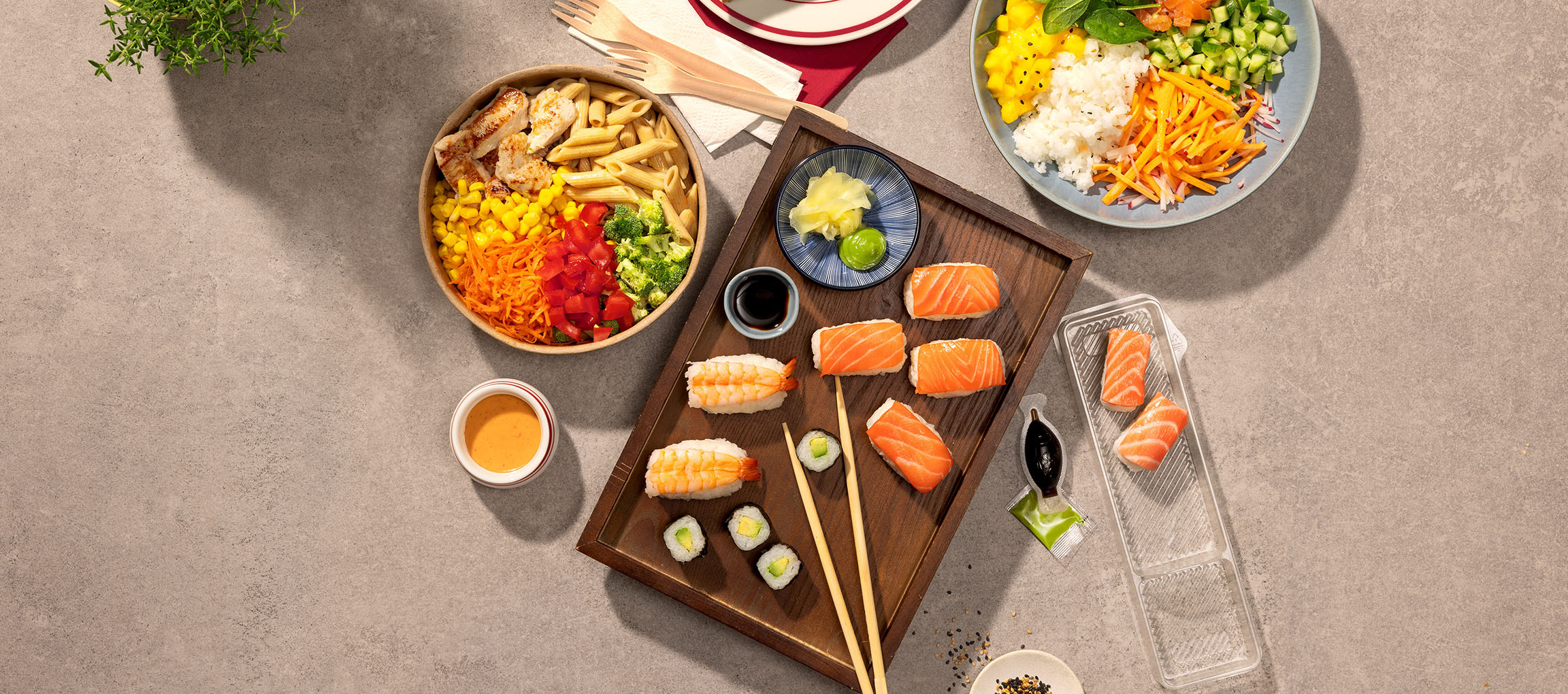 Verschiedene Gerichte: Nudel-Hähnchen-Bowl, Sushi und eine Poke Bowl auf einem Tisch.
