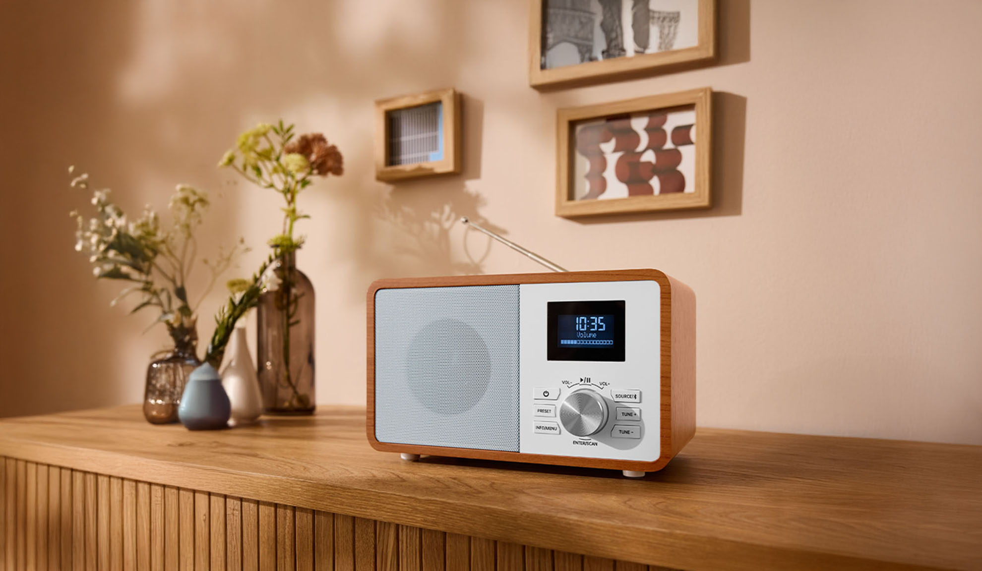 Ein digitales Holzradio auf einer Kommode, mit Vasen und Bilderrahmen im Hintergrund.