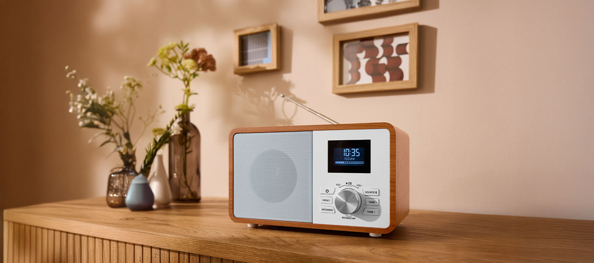 Ein digitales Holzradio auf einer Kommode, mit Vasen und Bildern an der Wand.