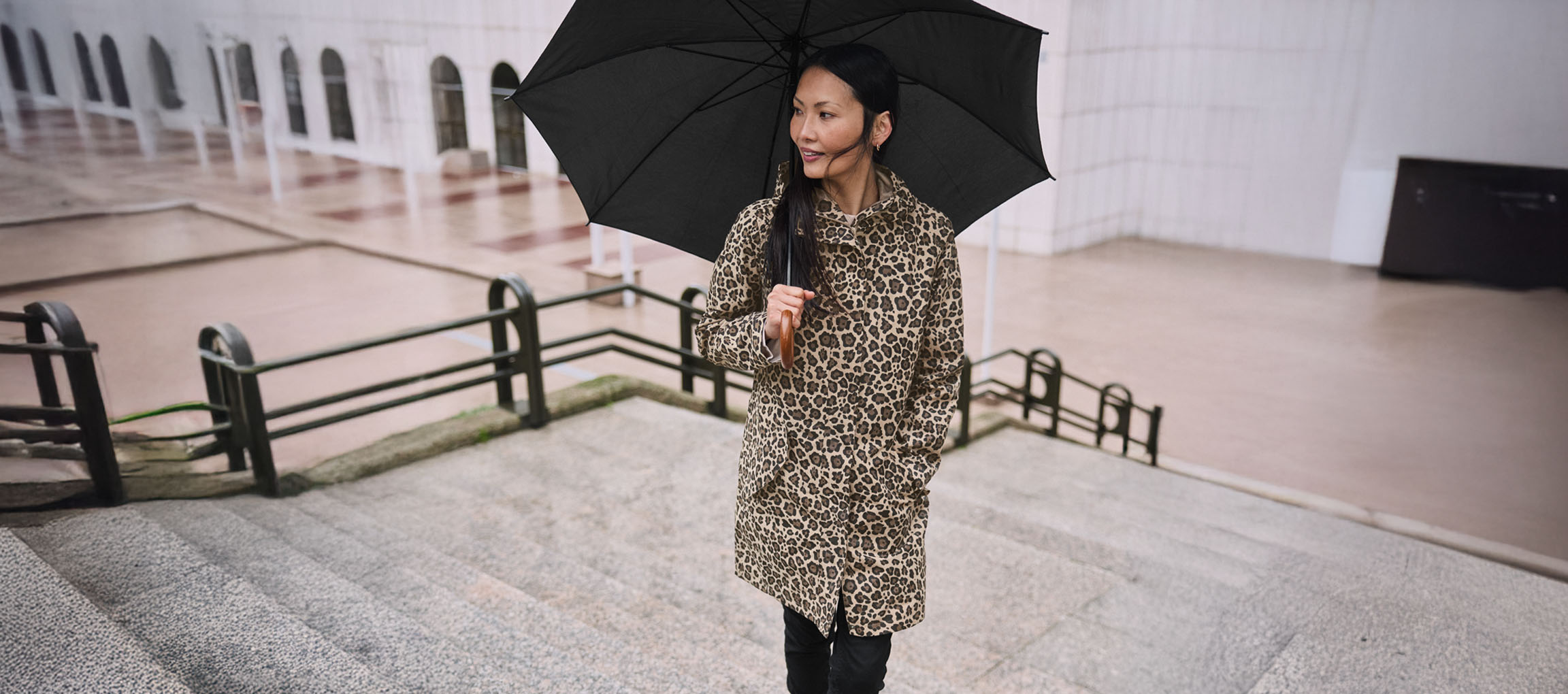 Frau im Leopardenmantel mit Regenschirm auf Treppe.