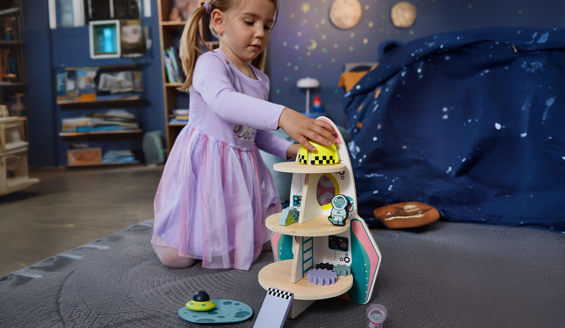 Ein Mädchen spielt mit einer Spielzeugrakete und Weltraumzubehör in einem Themenzimmer.