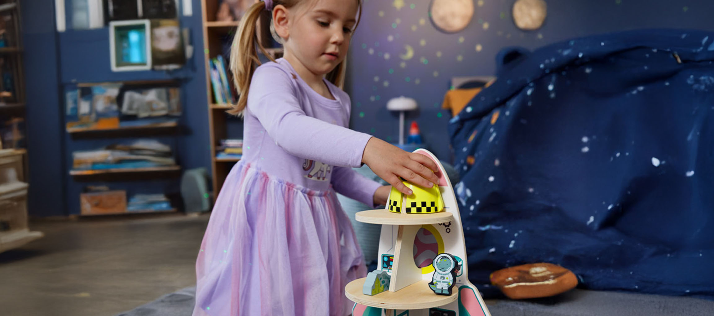 Kleines Mädchen spielt mit einem Raumschiff-Spielzeug in einem Weltraum-Zimmer.