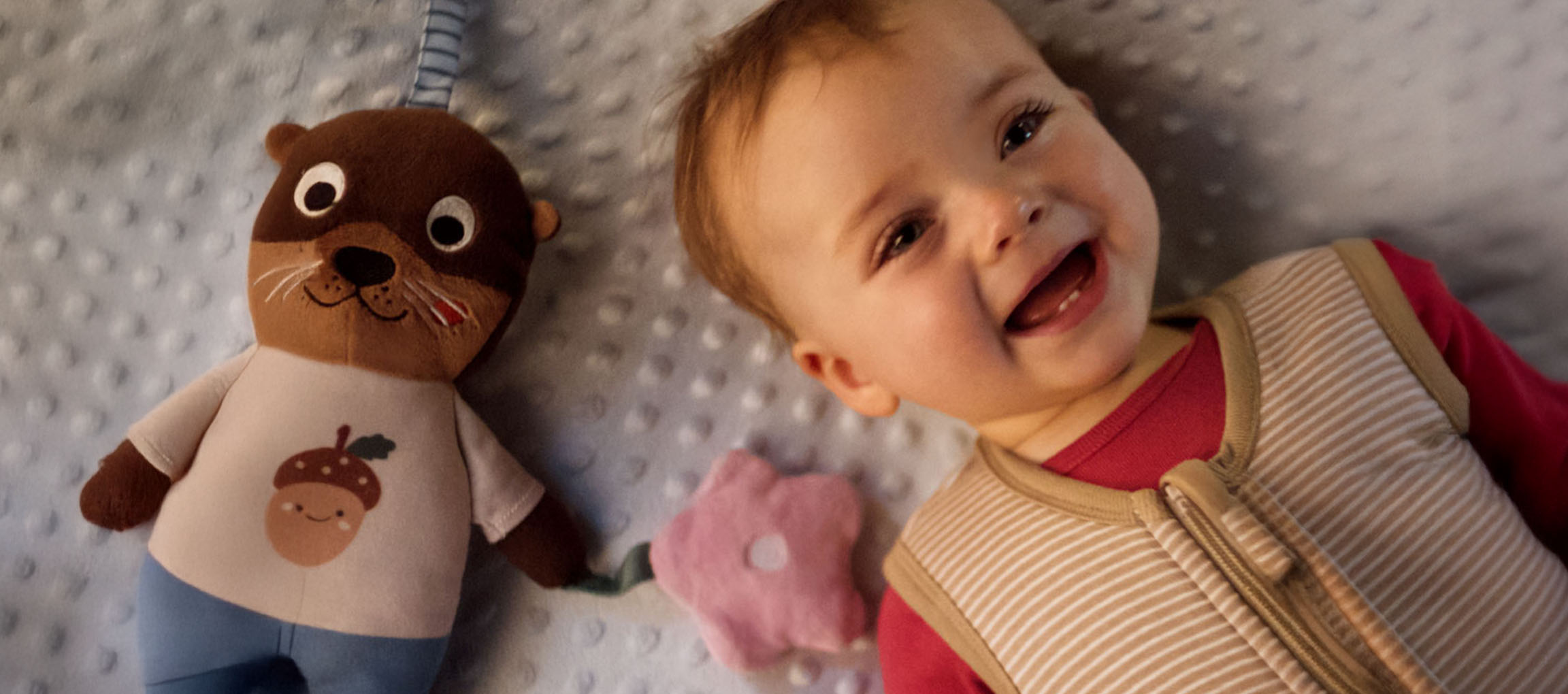 Lächelndes Baby und ein Plüschtier mit einer Eichel auf dem Bauch.