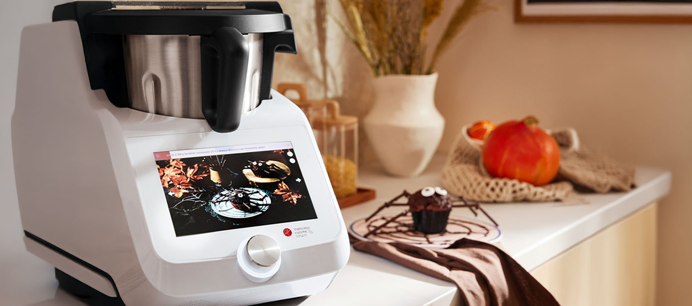 Küchenmaschine mit Touchscreen zeigt Halloween-Rezept, neben einem Spinnen-Muffin.