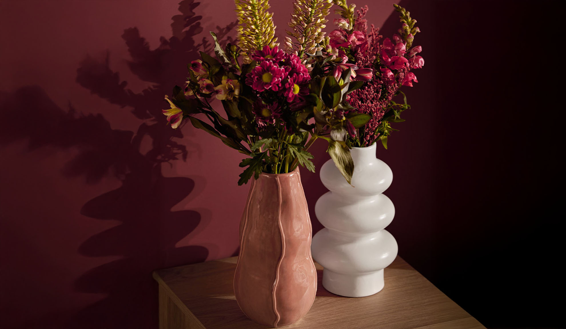 Zwei Vasen mit bunten Blumen auf einem Holztisch.