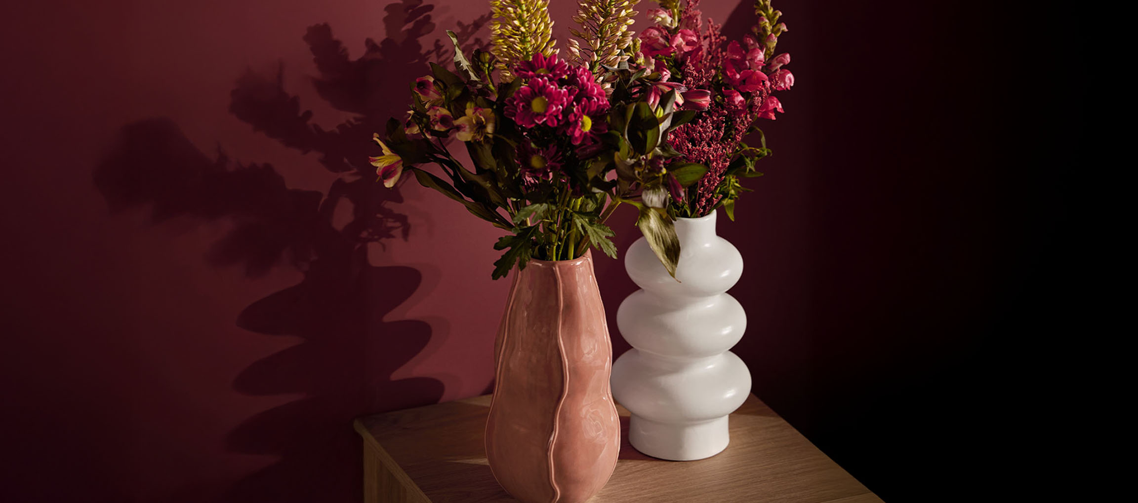 Zwei Vasen mit Blumen, eine rosa und eine weiße, auf einer Holzoberfläche.