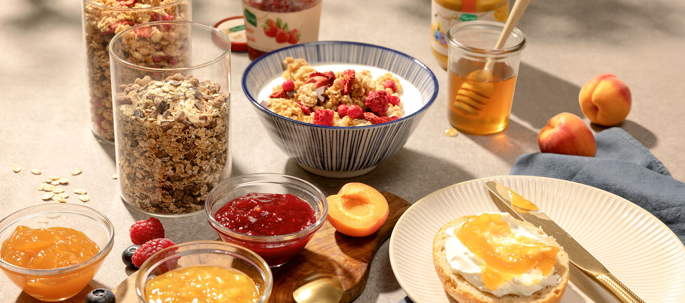 Frühstück mit Müsli, Milch, Honig, Marmeladen und Brötchen mit Frischkäse.