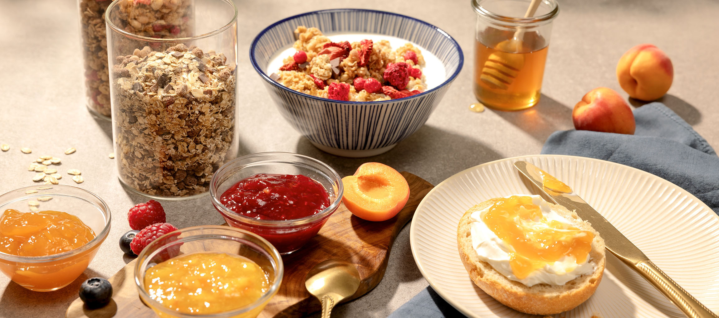 Frühstück mit Müsli, Marmelade, Honig und Brot mit Frischkäse und Marmelade.