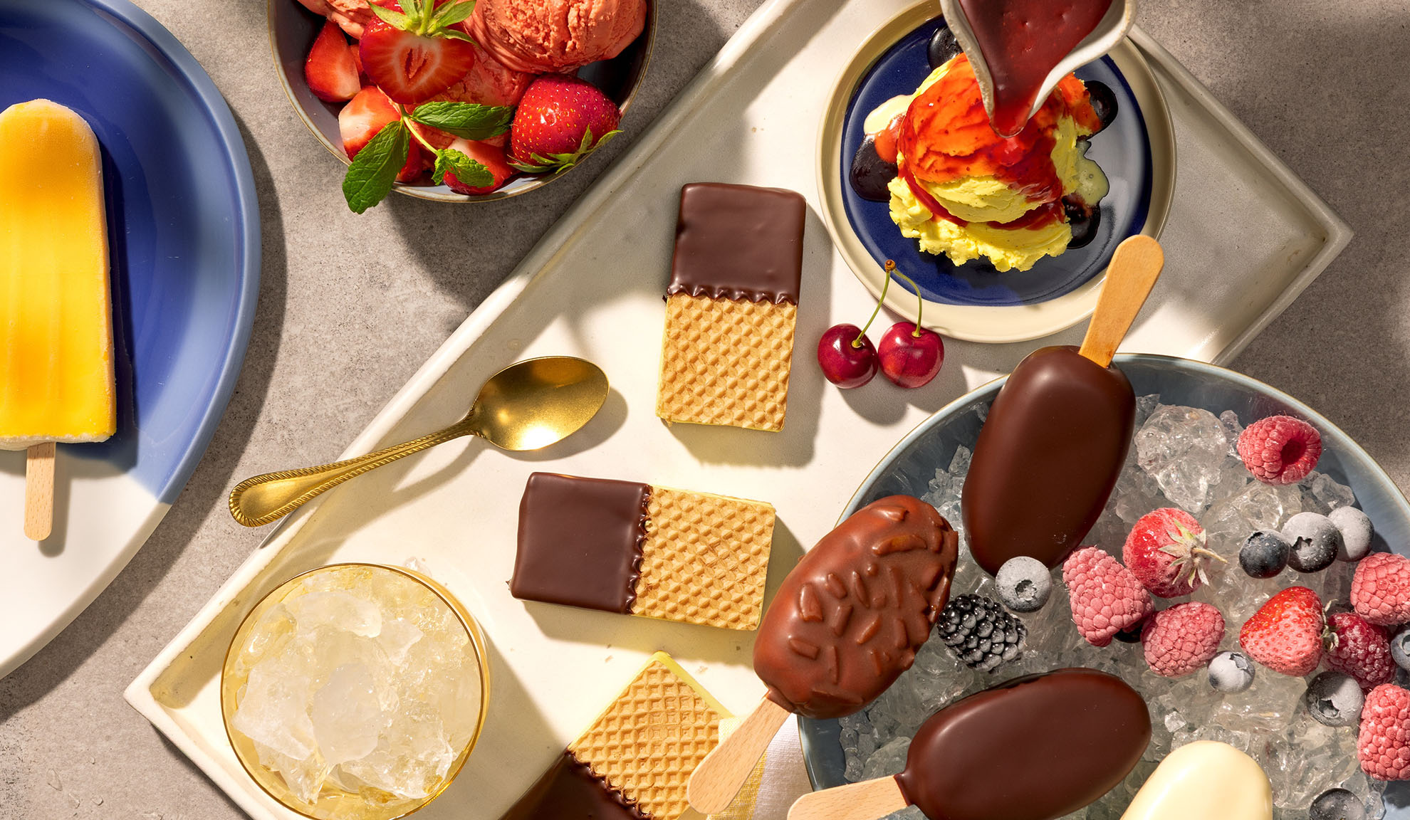 Sortiment an Eis am Stiel, Waffeln und Beeren auf einem Tablett.