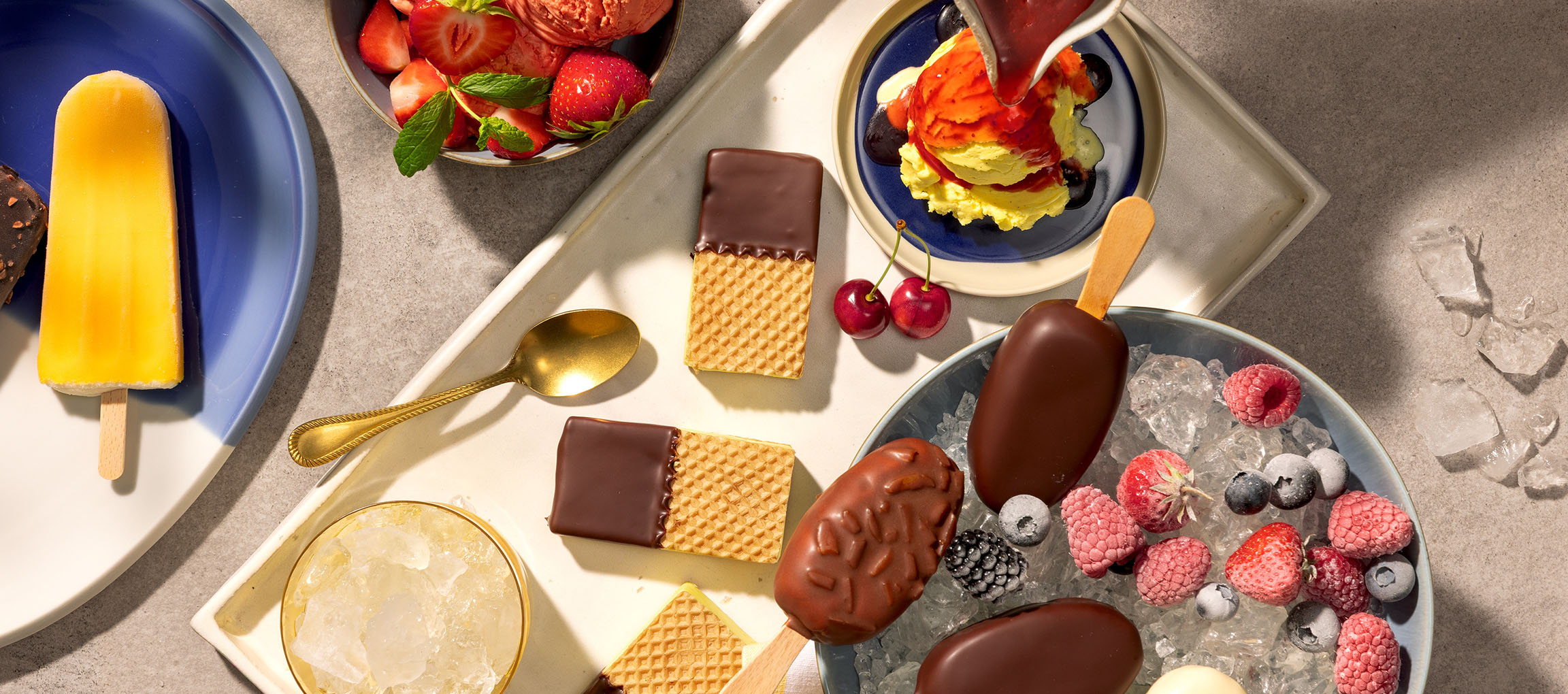 Sortiment aus Eis am Stiel, Eiskugeln und schokoladenüberzogenen Waffeln mit Beeren.