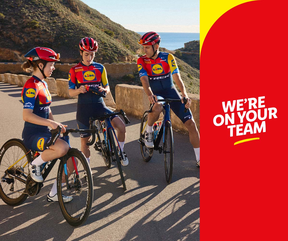 Drei Radfahrer*innen im Lidl-Trek-Team-Trikot posieren mit ihren Rennrädern auf einer Küstenstraße.
