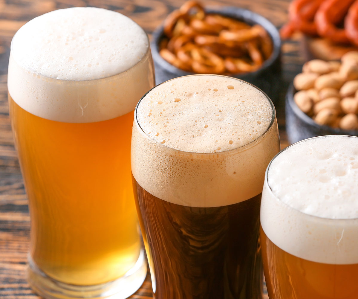 Verschiedene Biere stehen auf einem Holztisch. Im Hintergrund sind Snacks zu sehen.