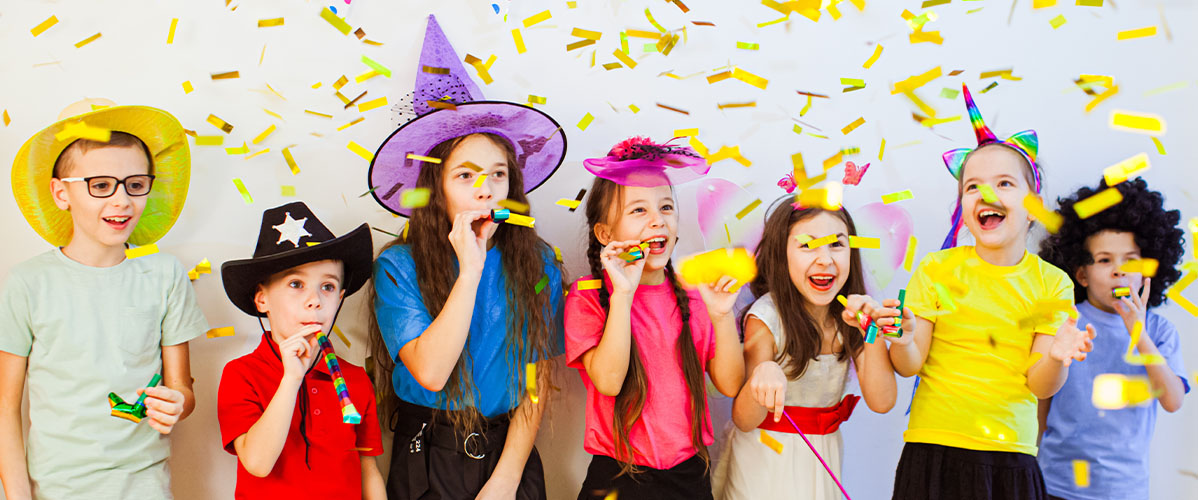 Verkleidete Kinder feiern Fasching und goldenes Konfetti fliegt in der Luft.