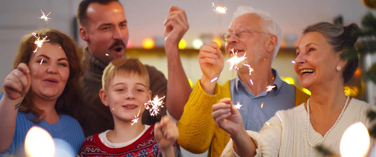 Fröhliche Familie steht beisammen und jeder hält einen angezündeten Sternspritzer in der Hand.