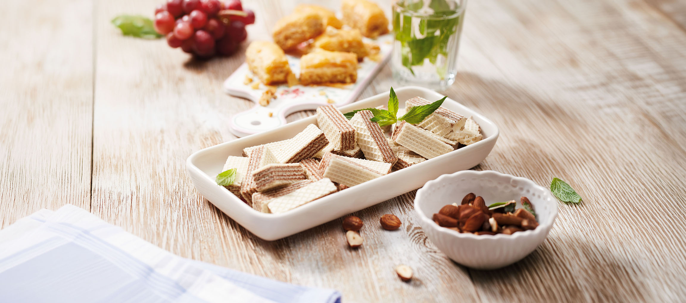 Waffelgebäck, Baklava, Trauben und Minzwasser auf einem Holztisch.