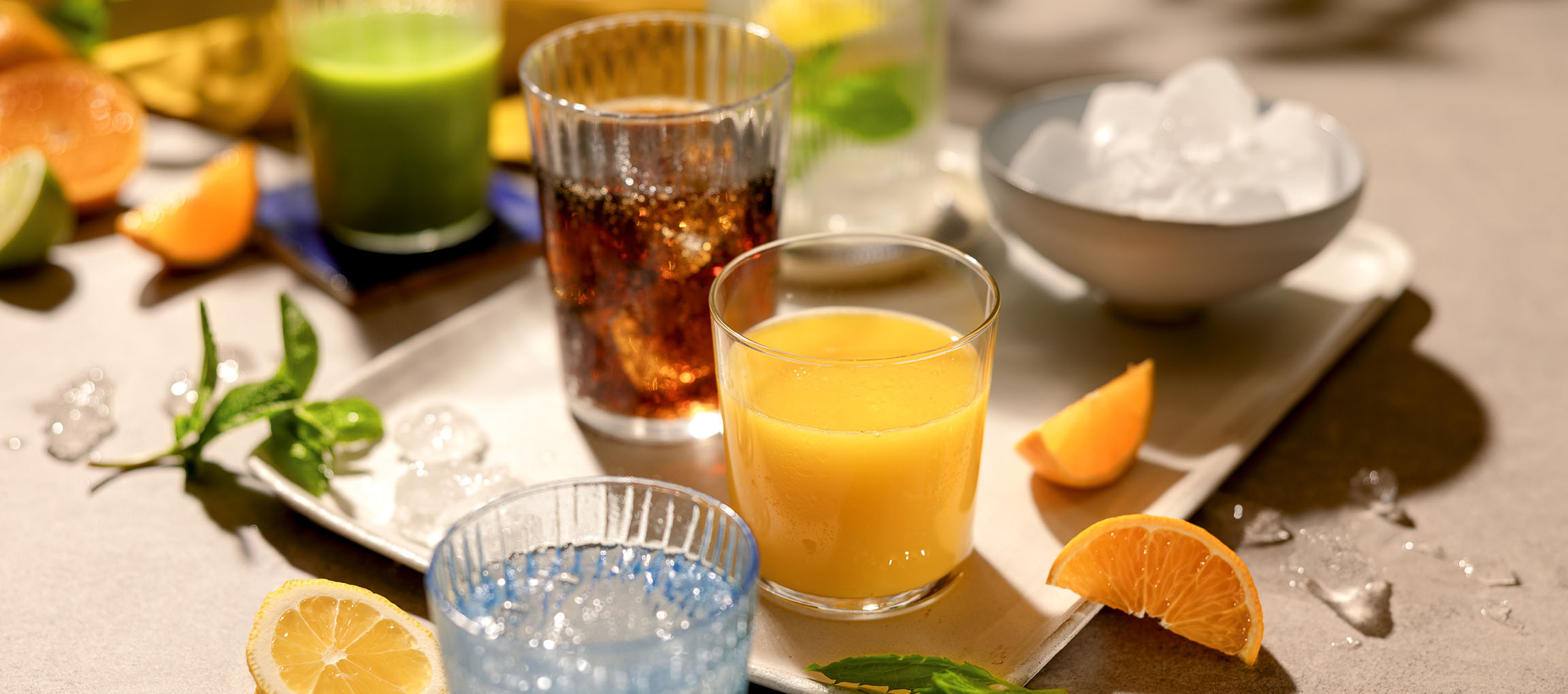 Verschiedene erfrischende Getränke und Früchte auf einem Tablett, darunter Orangensaft und Limonaden.