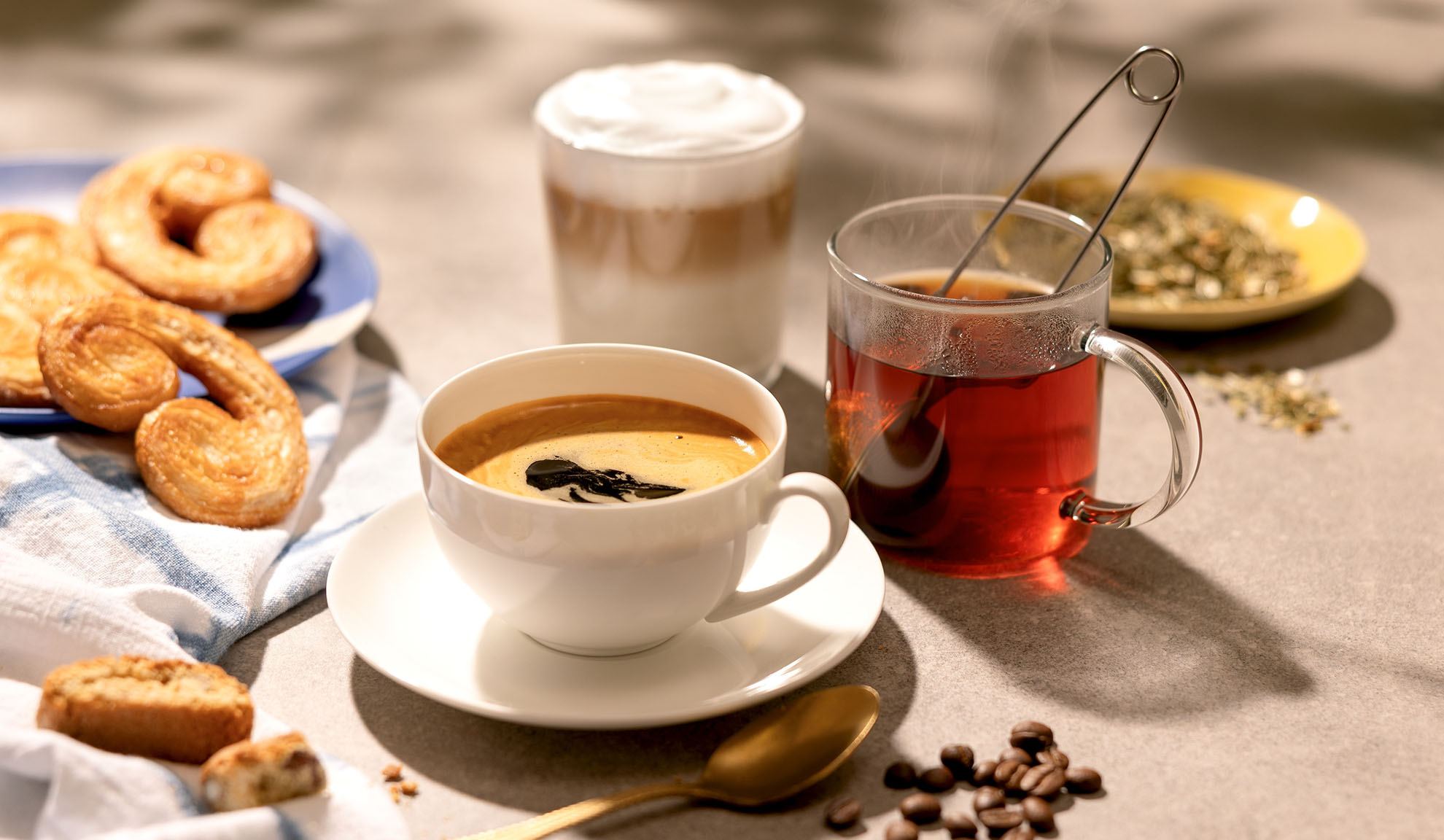 Kaffee, Tee und Latte mit Gebäck und Kaffeebohnen auf einem Tisch.