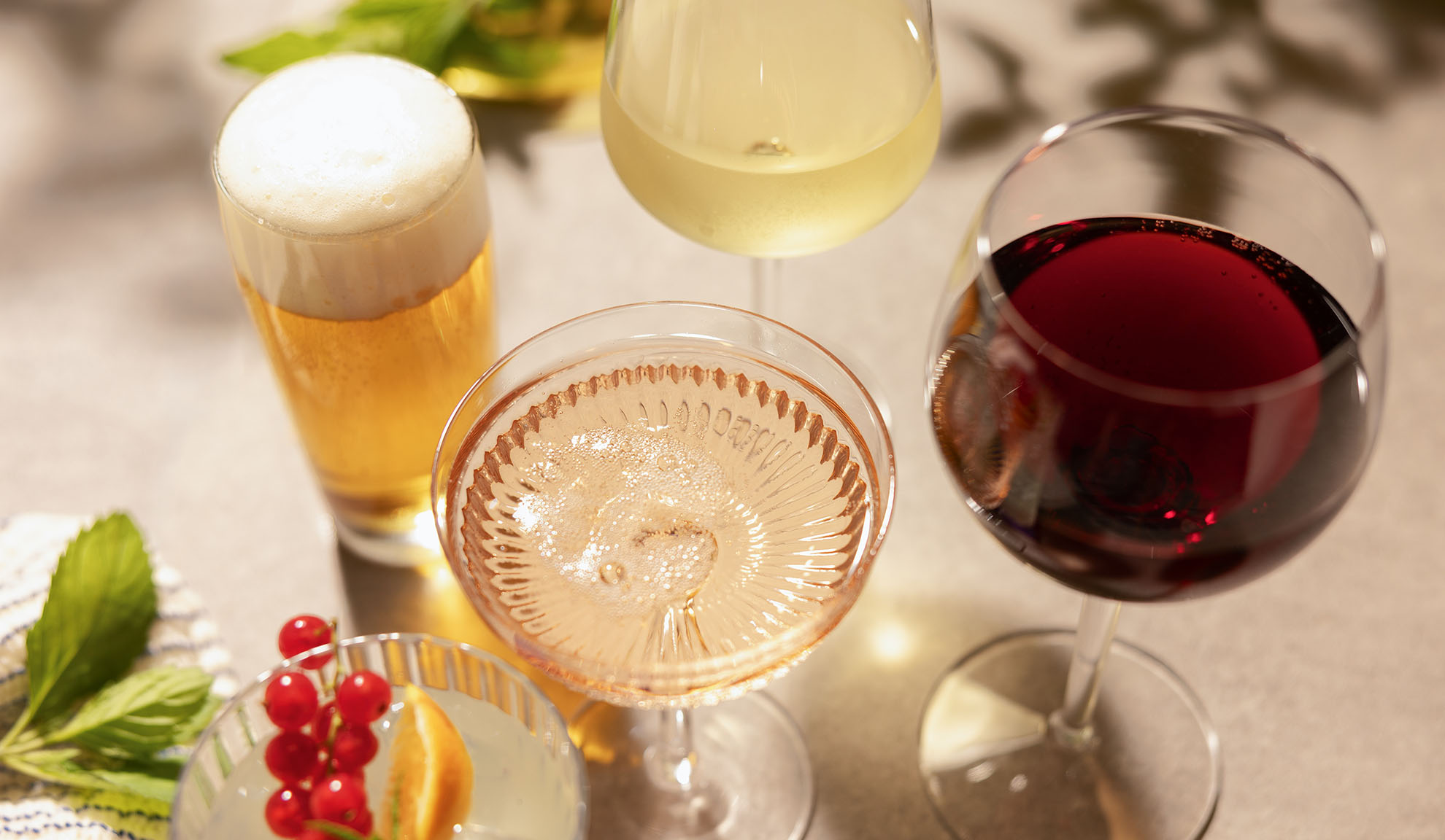 Gläser mit Bier, Weiß-, Rosé- und Rotwein, dazu ein Cocktail und Beeren.