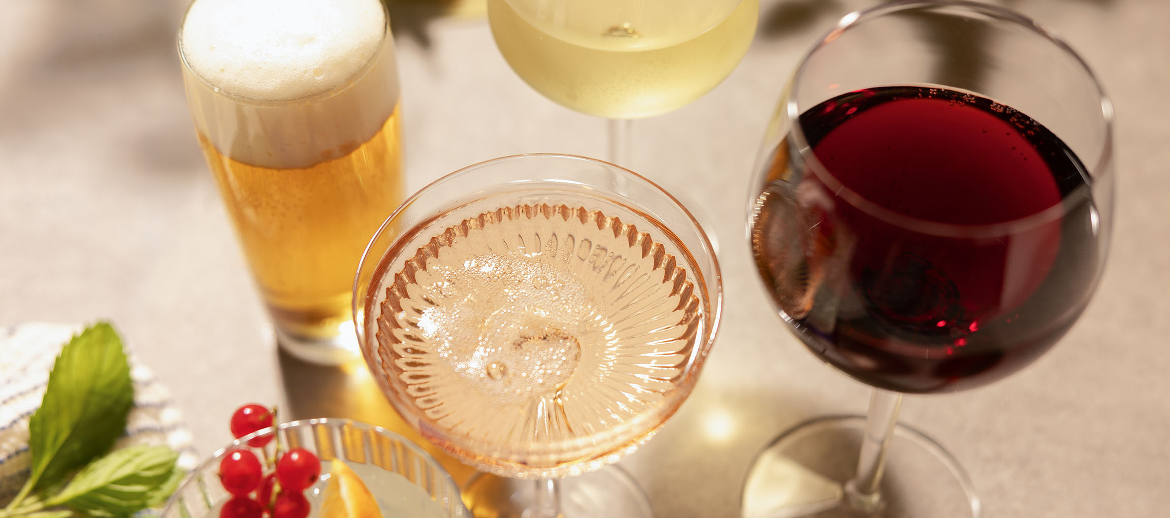 Bier, Roséwein und Rotwein in Gläsern, mit Beeren und Minze.
