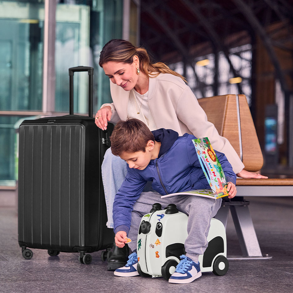 Frau und Kind mit großem schwarzem Koffer und Panda-Kinderkoffer am Flughafen.