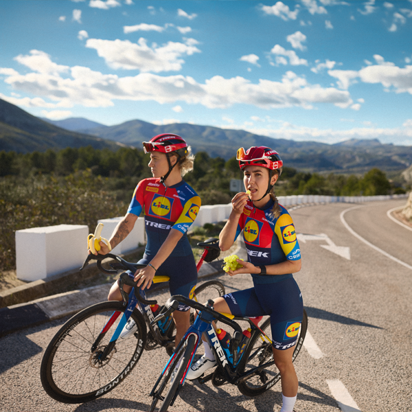 Zwei Radrennfahrerinnen des Teams Trek-Segafredo Lidl genießen eine Pause mit Obst.