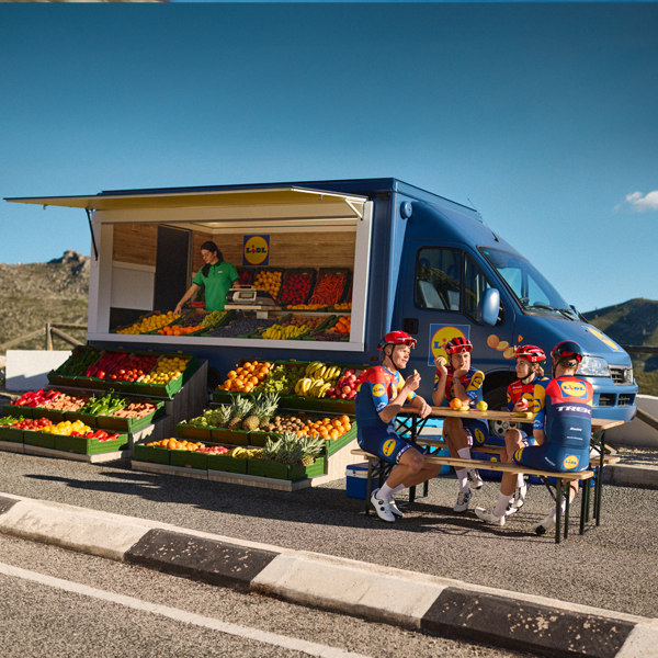 Radfahrer machen Pause an einem Lidl-Lkw voller Obst und Gemüse.