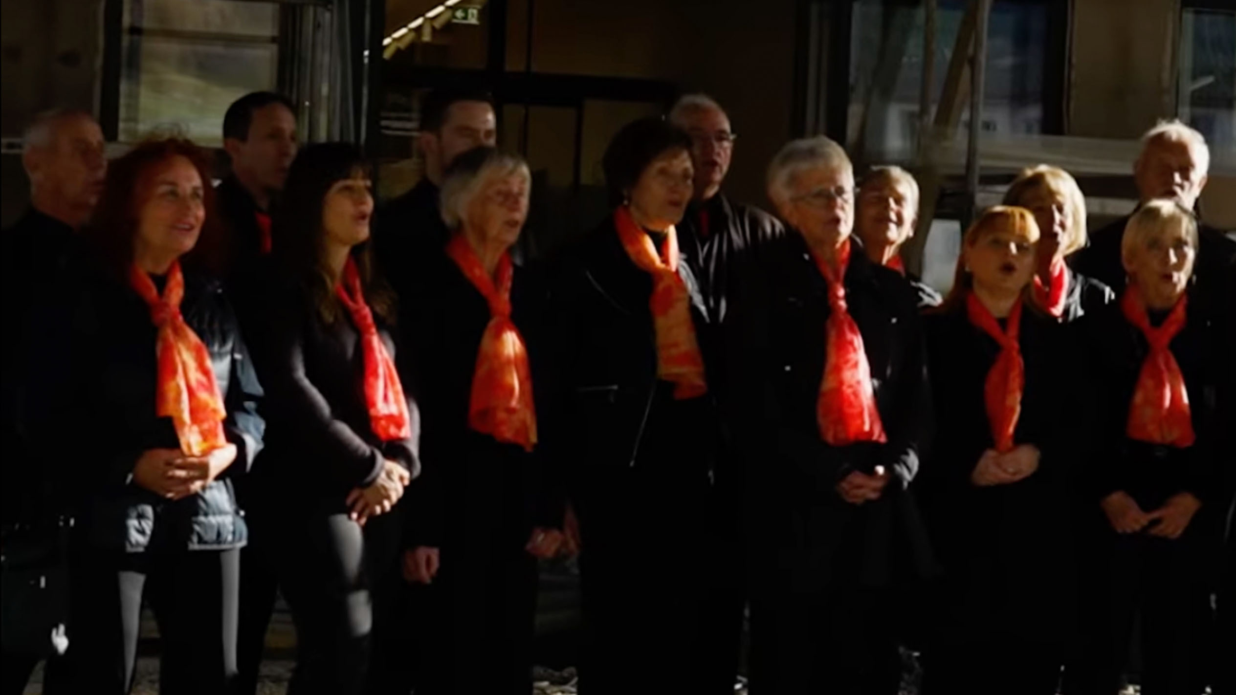 Chor singt, gekleidet in Schwarz mit orangefarbenen Schals