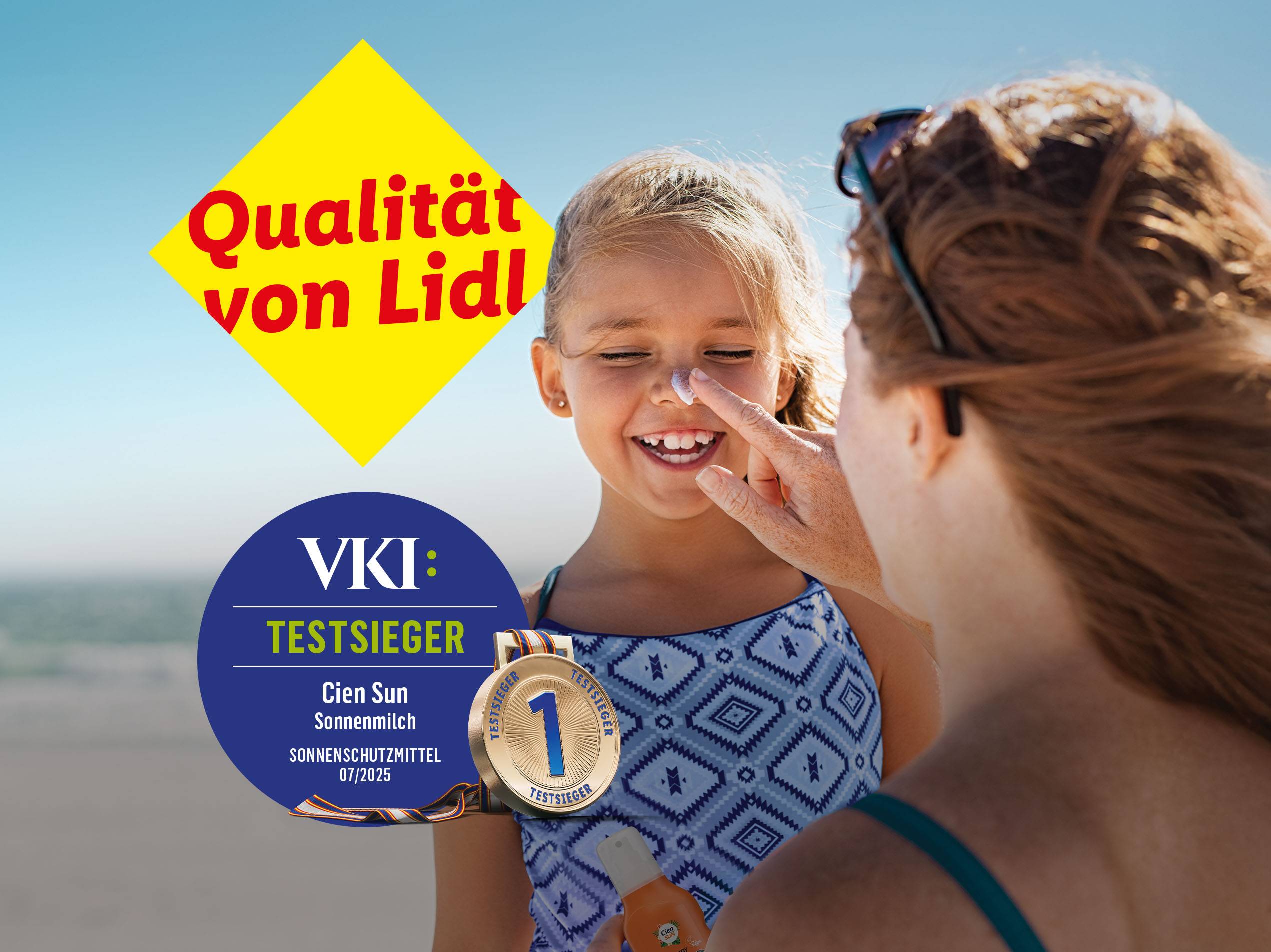 Eine Mutter cremt ihrer Tochter am Strand mit Sonnencreme ein. Unten links VKI Testsiegel für Cien Sun Sonnenmilch. Textzusatz: Qualität von Lidl. 