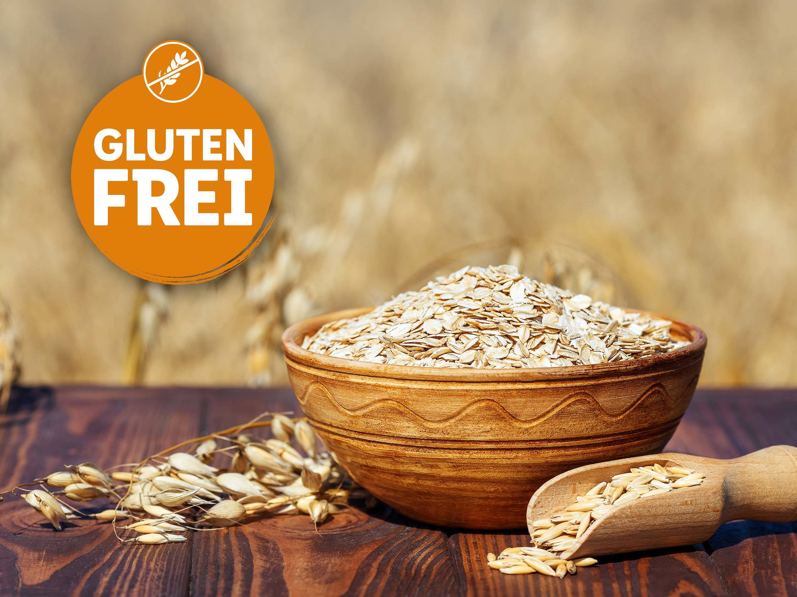 Eine Schale glutenfreie Haferflocken steht auf einem Holztisch, neben einer kleinen Holzschaufel mit Haferkörnern.