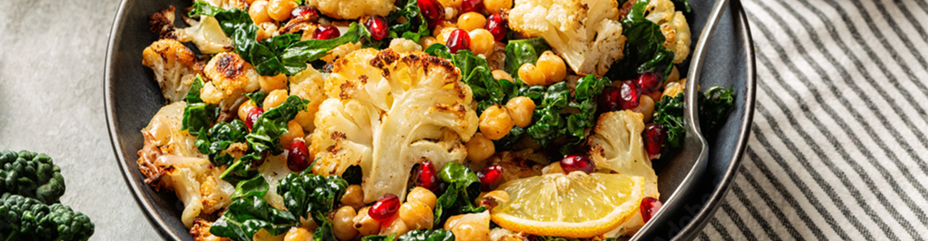 Gerösteter Blumenkohl, Grünkohl und Kichererbsen mit Granatapfelkernen und Zitrone in einer Schüssel.