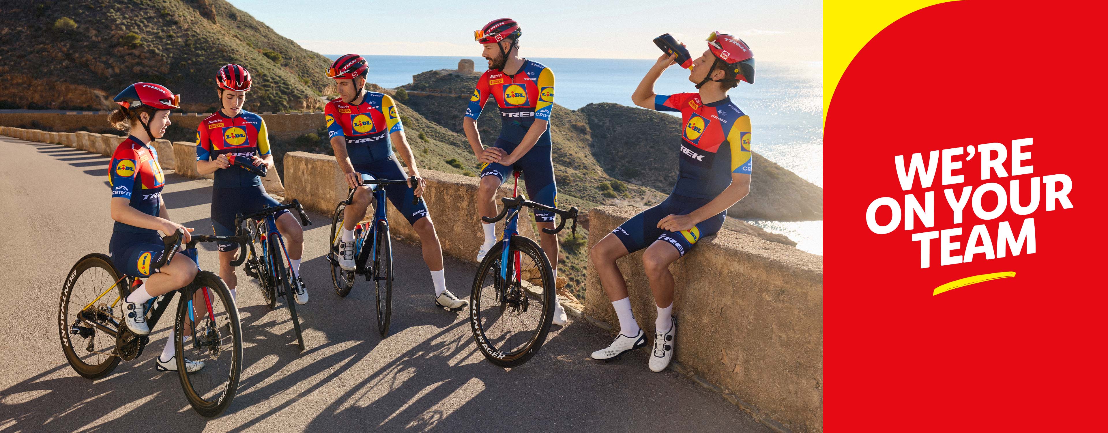 Drei Radfahrer*innen im Lidl-Trek-Team-Trikot posieren mit ihren Rennrädern auf einer Küstenstraße.