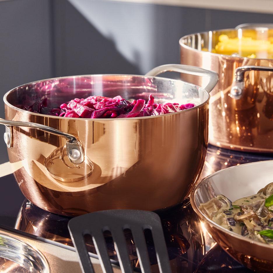 Kupfertöpfe mit Rotkohl und Nudeln auf einem Kochfeld, mit einer Schale Pilzragout.
