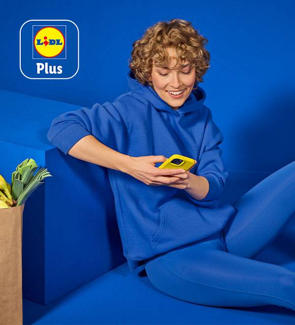 Eine Frau in einem blauen Hoodie nutzt die Lidl Plus App auf ihrem Smartphone.