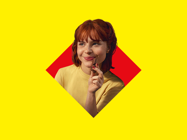 Eine lächelnde rothaarige Frau hält eine Schokolade vor gelbem und rotem Hintergrund.