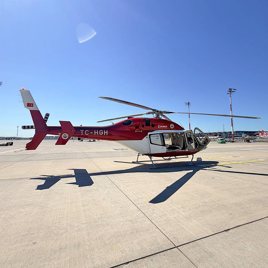 Roter und weißer Hubschrauber auf einem Rollfeld unter blauem Himmel.