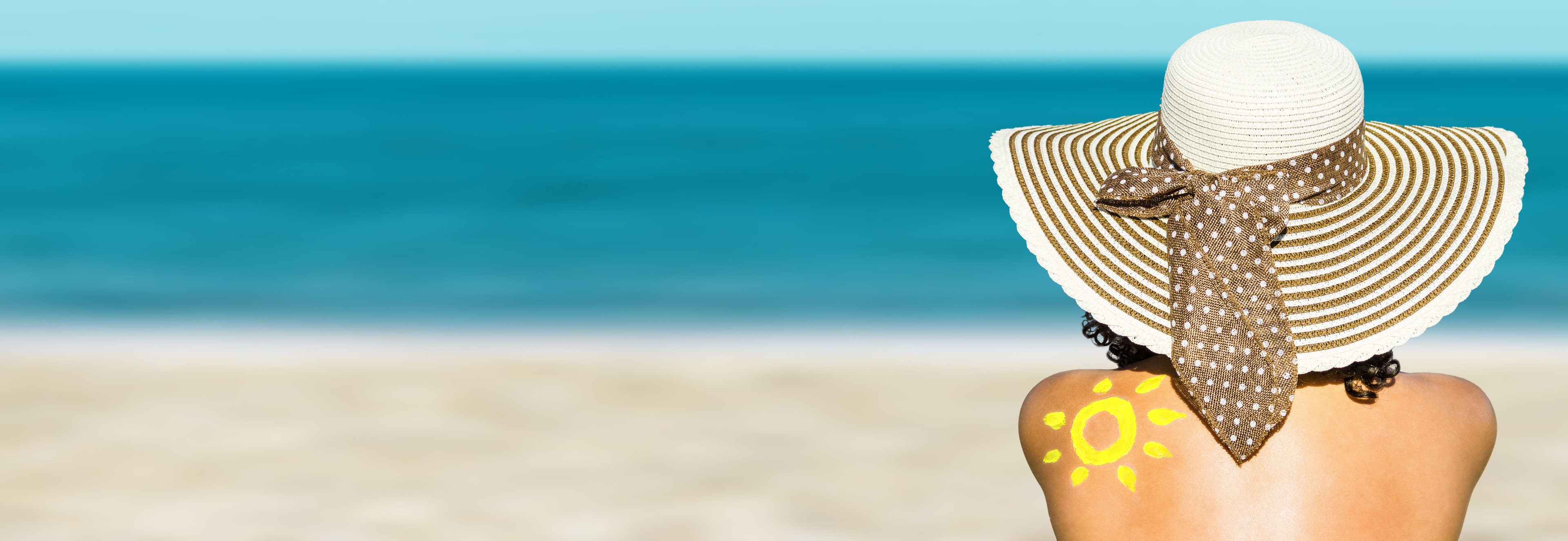 Frau mit Sonnenhut und Sonnencreme-Sonne auf dem Rücken am Strand.