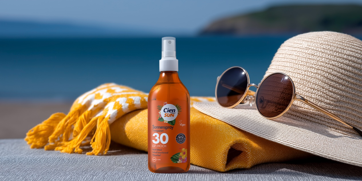 Sonnenspray, Sonnenhut und Sonnenbrille am Strand mit Meer im Hintergrund.
